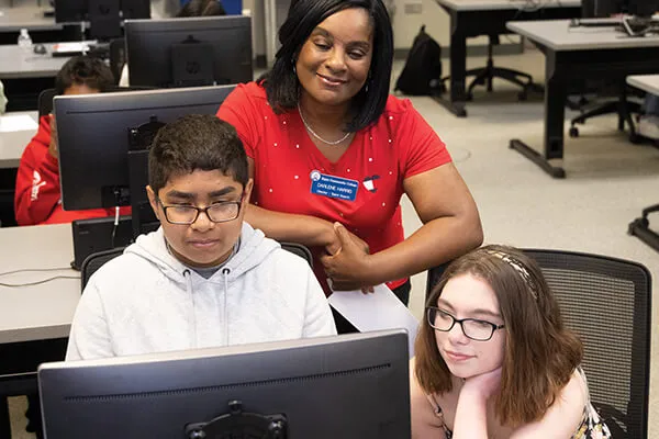 A faculty member helping students at a computer.