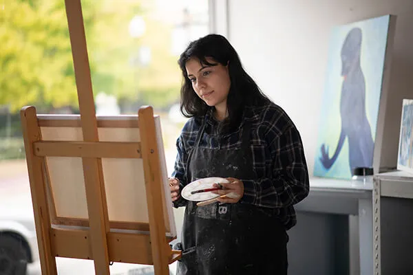 A student painting a canvas on an easel.