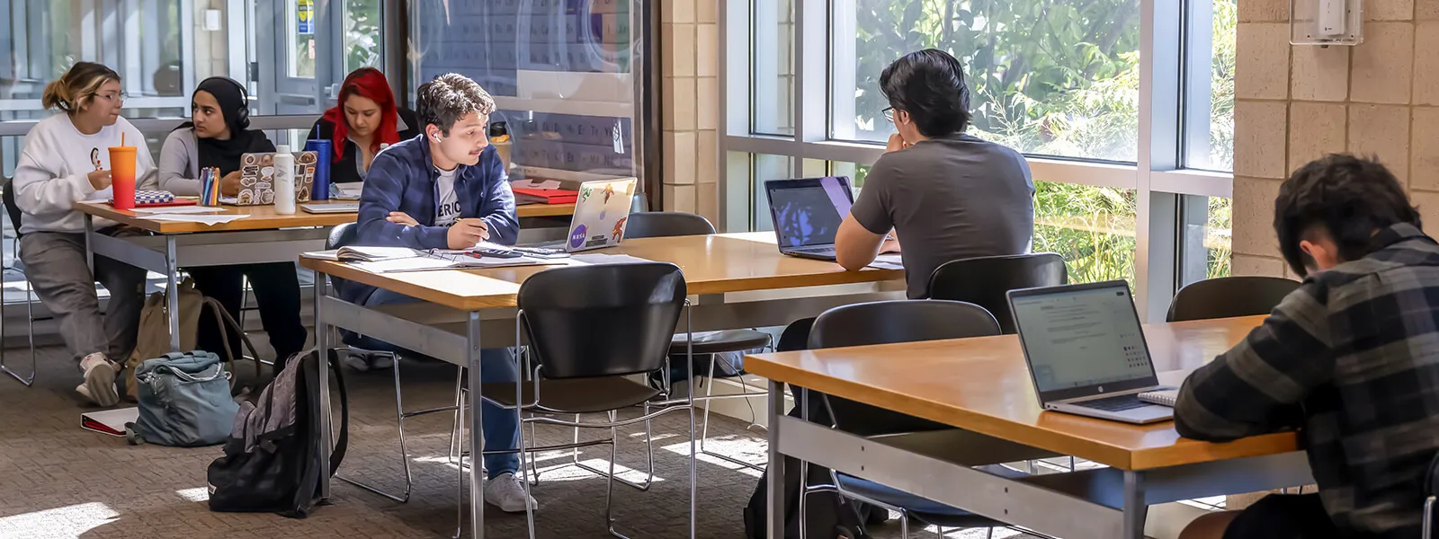 Students studying at tables in a well lit area of the college.