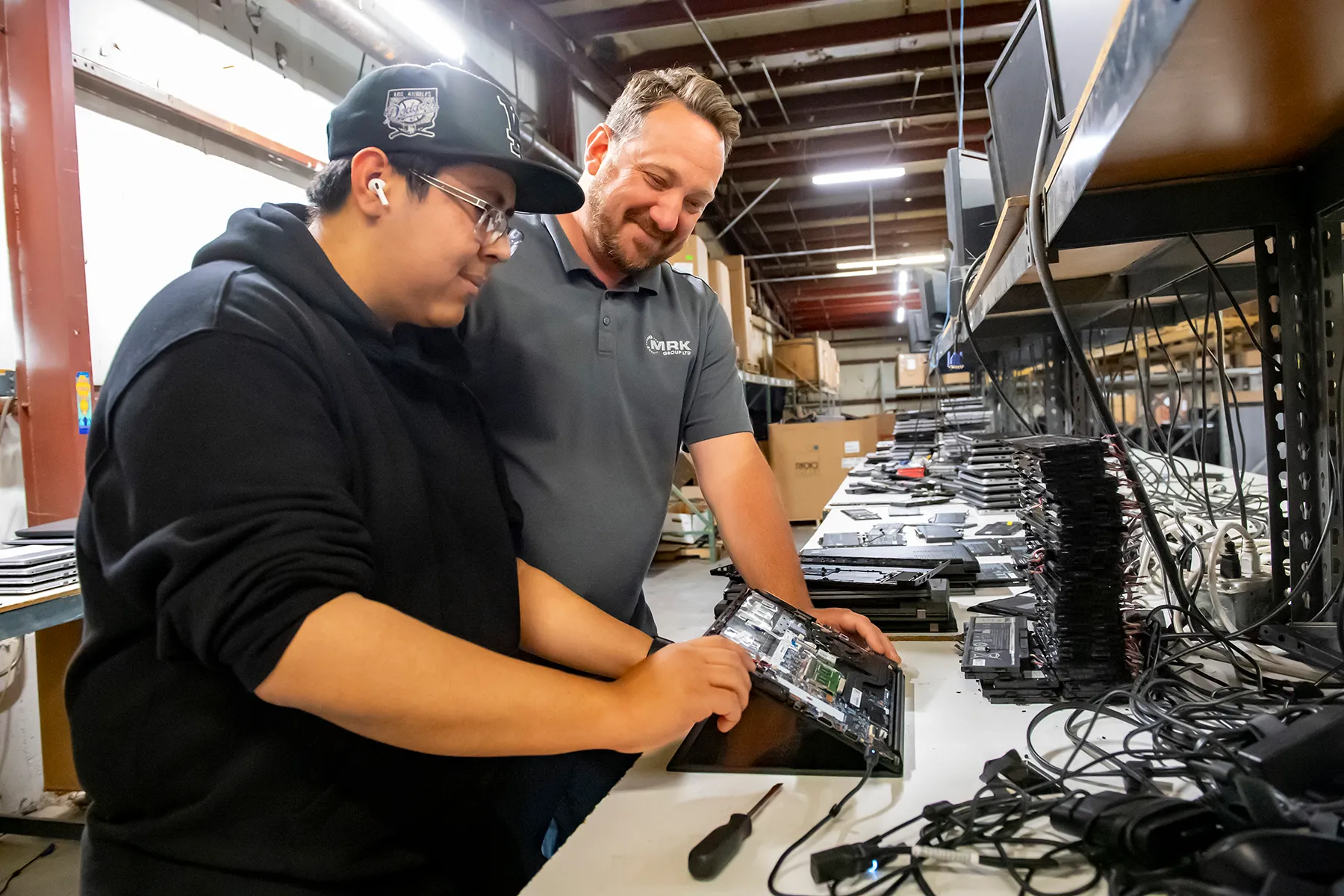 Student Joseph Patino works on a computer repair with his internship mentor, Joe Ruffalo, looking on.