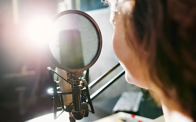 A student speaking into a microphone while recording a podcast