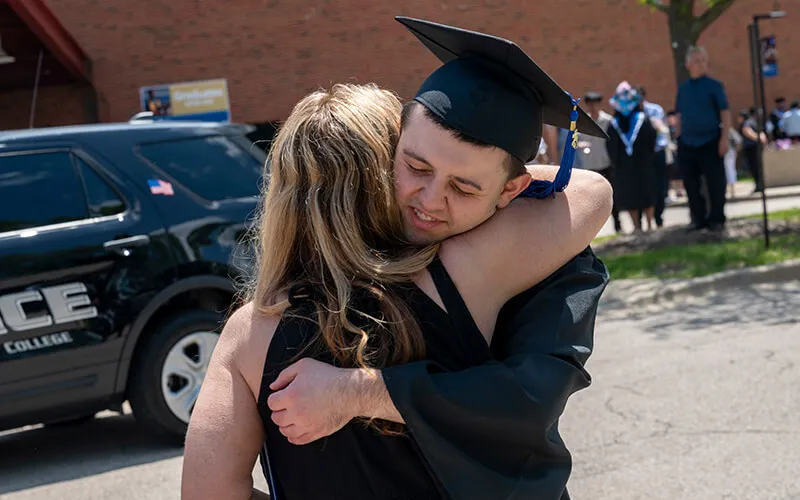 A grateful student wearing a cap and gown hugging his mother.