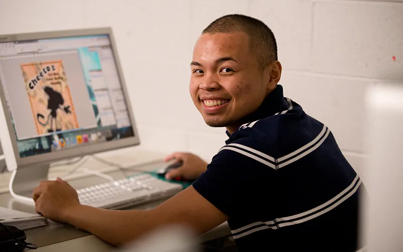 A student smiling while sitting at computer with his hands on a keyboard