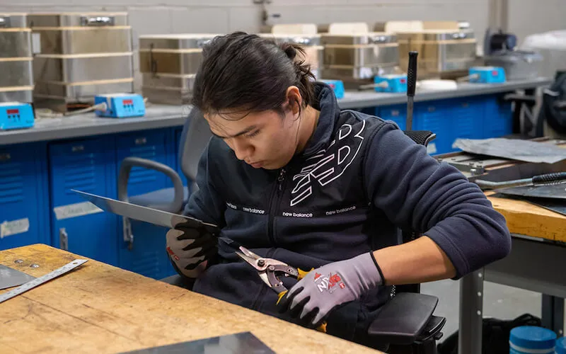 A student adjusting a piece of metal with a pair of handheld metal cutters