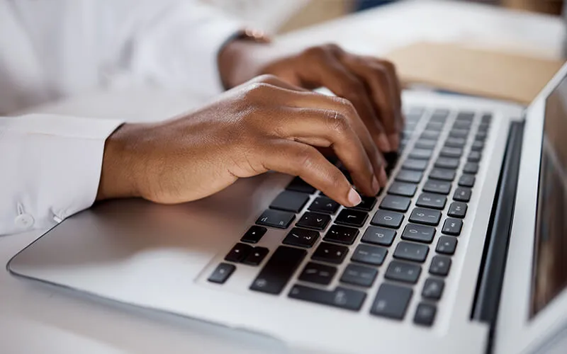 A close up of the hands of student of color typing on a laptop