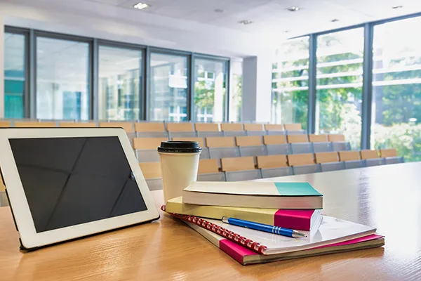 Digital tablet, books and cup of coffee on table in classroom