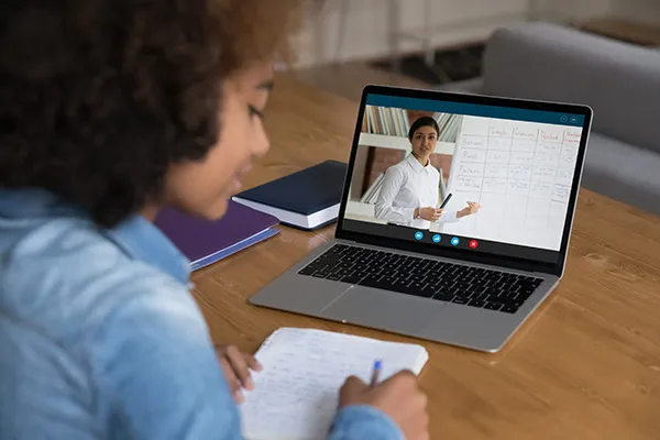 African teenager girl studying online seated at desk with laptop