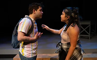Two students are interacting on stage in a dark room