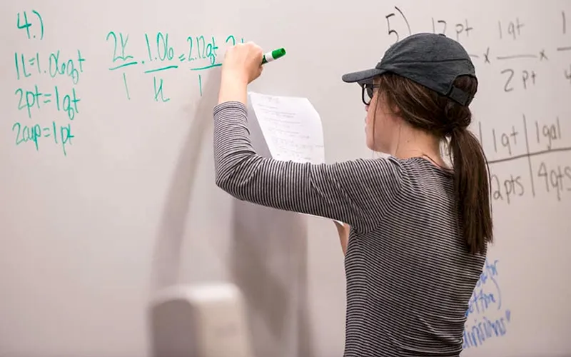A female student is writing equations on a dry-erase board.