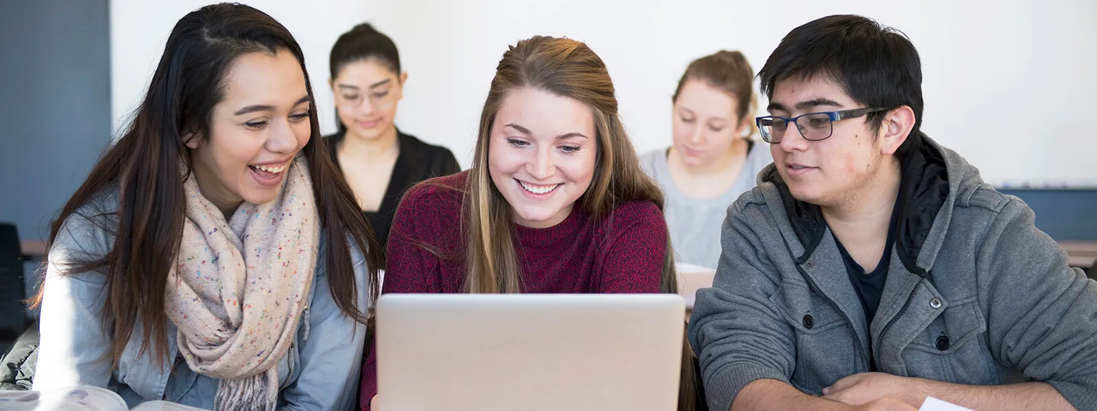 Students gathered around a laptop in a classroom.