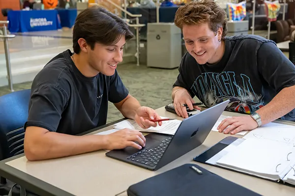 Two students sitting together, focused on a laptop while studying