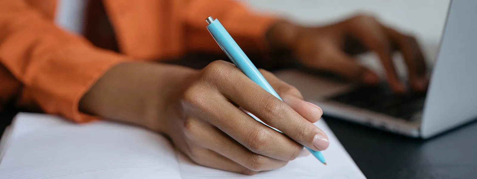 Close-up shot of student hand holding pen and writing in notebook.