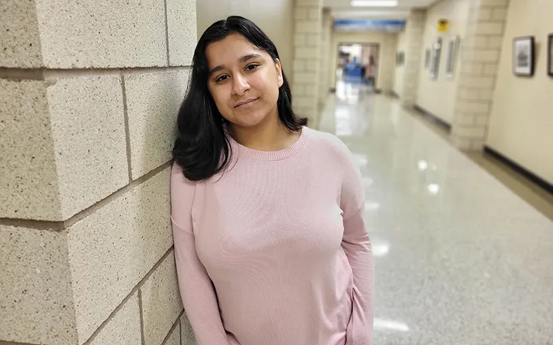 Una estudiante con un jersey rosa se apoya contra una pared en el interior del Edificio D del campus de ECC.