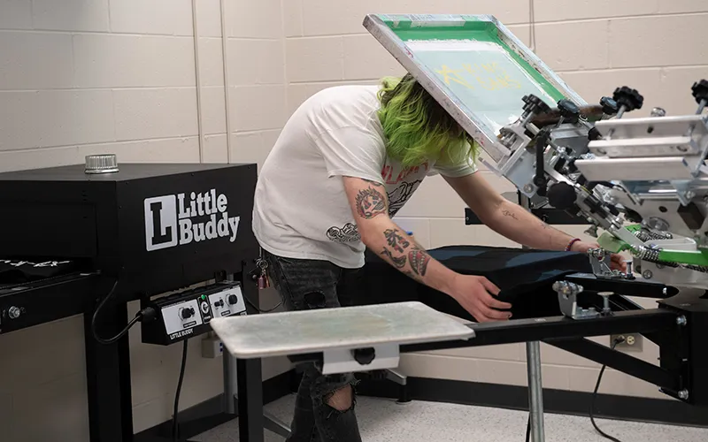 An art and design student demonstrates screen printing a t-shirt in the print shop.