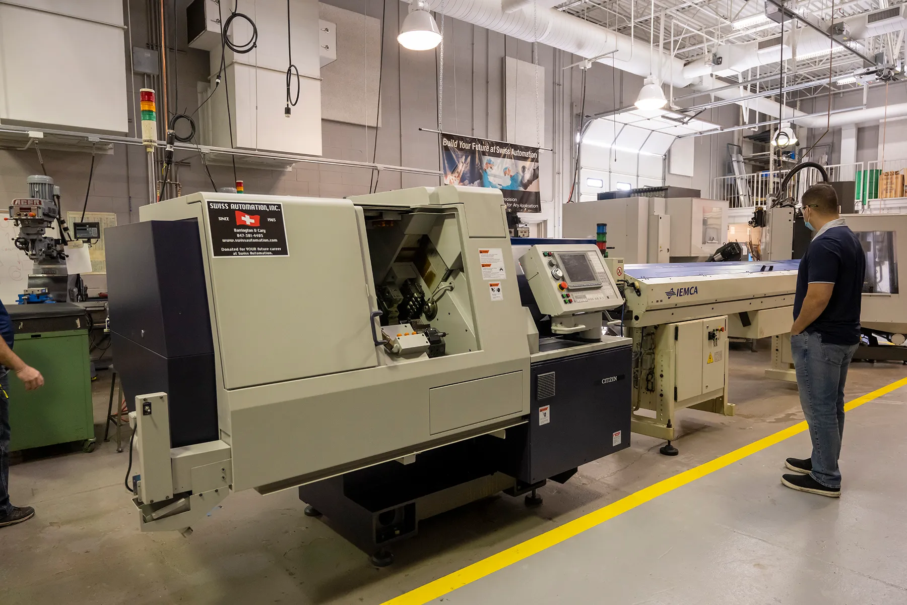 Alejandro Murillo, instructor of IMT/CIM, admires the 9-axis machine donated by Swiss Automation, Inc