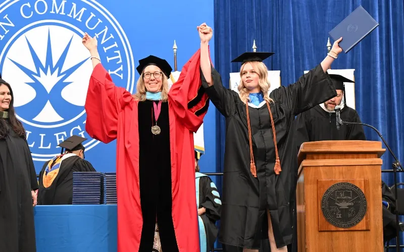 ECC President Peggy Heinrich and student put their hands up together in celebration on stage at a commencement ceremony on May 16, 2026.
