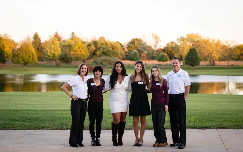 [From left to right]: Robin Seigle, Solis Jaime, Juliana Arroyo, Leah Foerster, Gianna Deutsch, and Mark Seigle pose together for a photo in front of ECC's Spartan Lake.