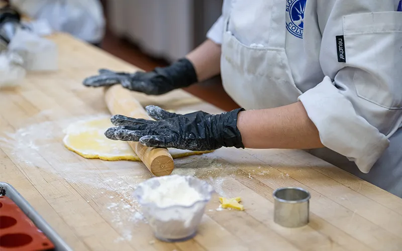 Person working in the kitchen, rolling dough.