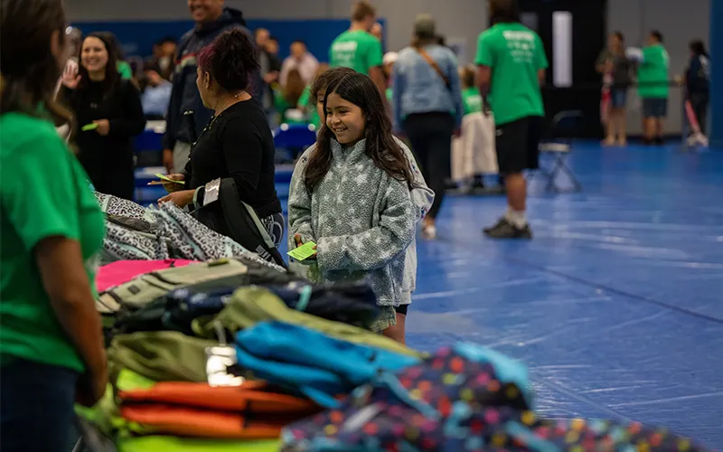 A child smiles at the tables of backpacks at the 2026 Project Backpack school supply giveaway event.