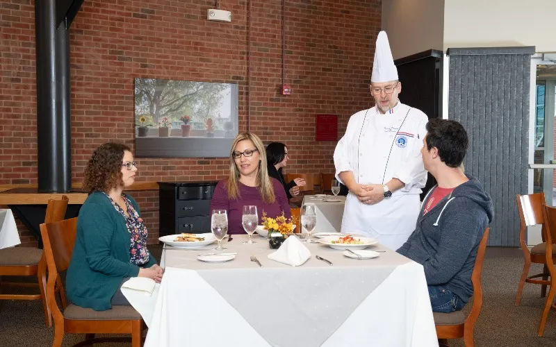Three people dine at ECC's Spartan Terrace restaurant while a chef talks to one individual.