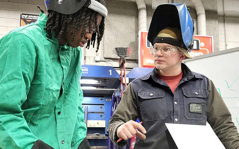 ECC Instructor and Alum Tom Limberis talks with a student in a welding classroom.