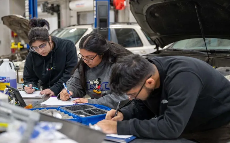 Estudiantes de automoción escribiendo sobre papel en un mostrador dentro de un garaje