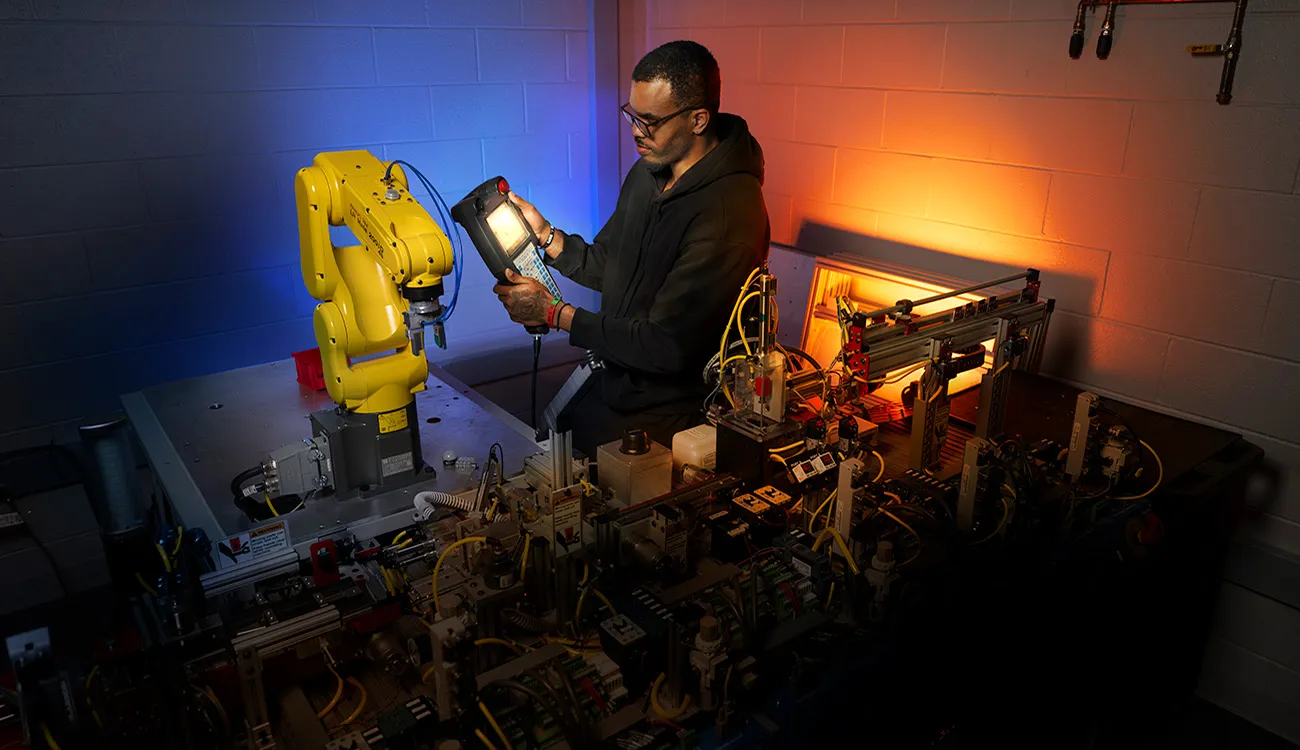Person uses a handheld controller to program or test a robotic arm within an industrial automation lab.