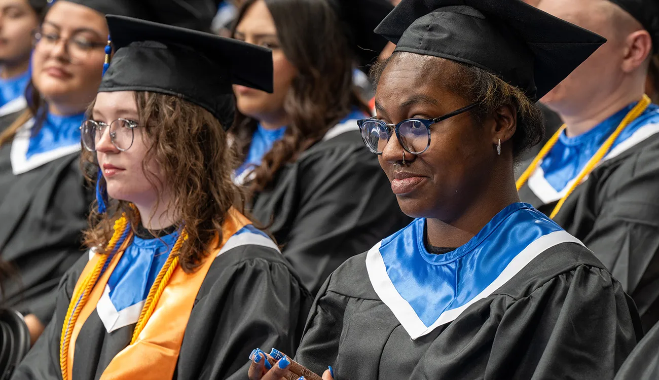 Graduates in caps and gowns sit together during a commencement ceremony, listening attentively as the event continues.