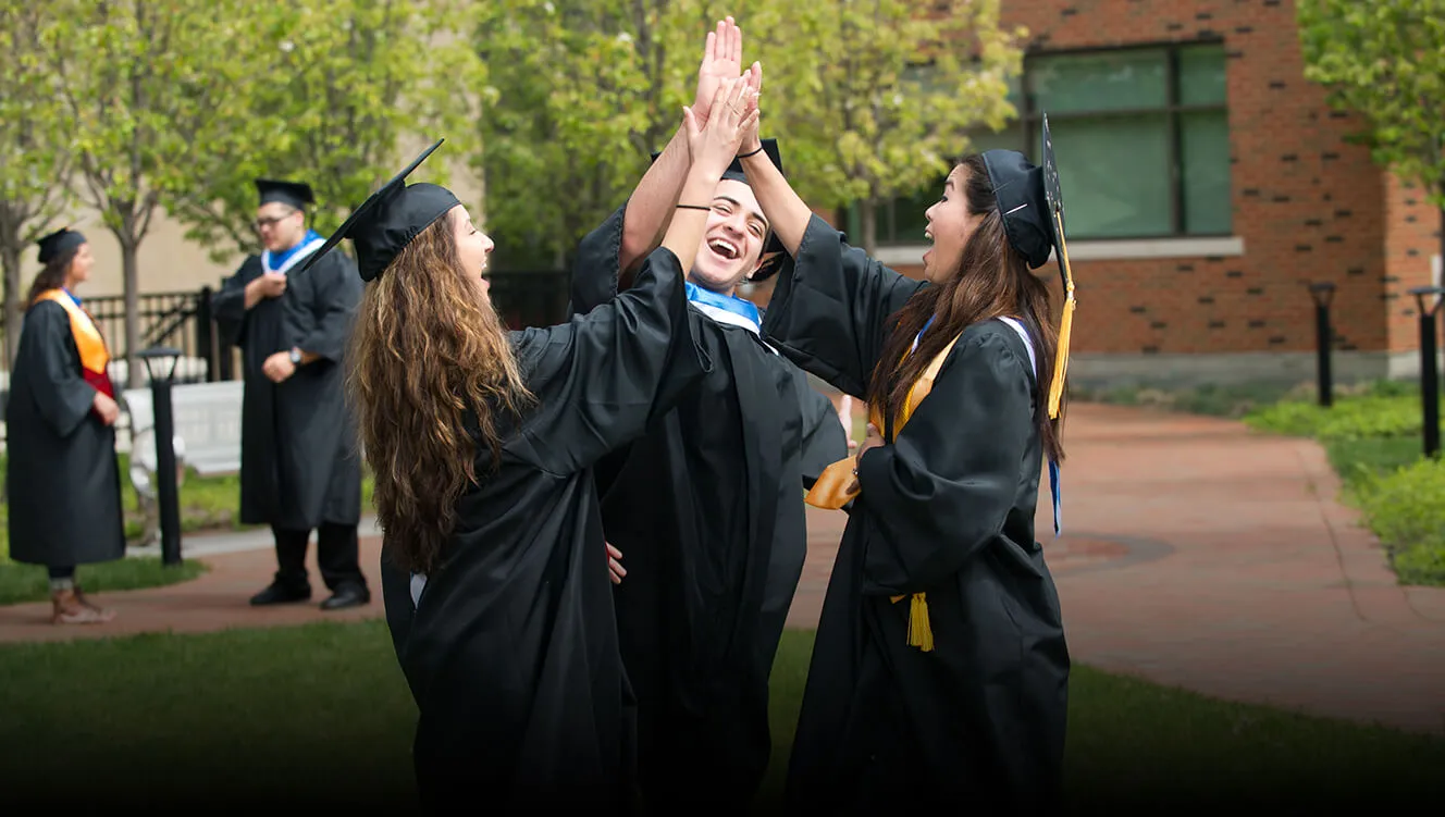 A group of students wearing caps and gowns giving each other high fives