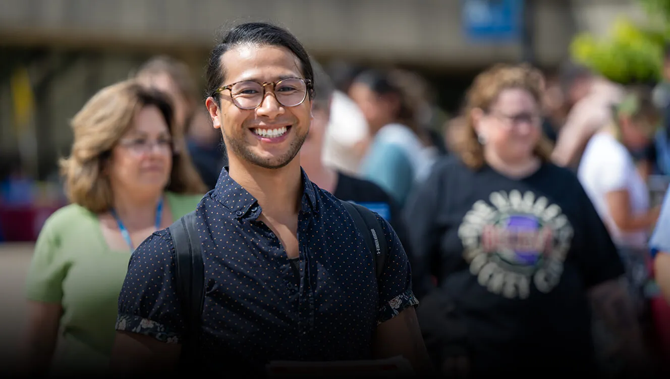 A male student walking outdoors through the crowd on campus