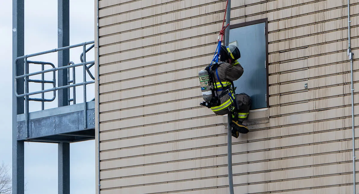 firefighter using fire hose to escape on the exterior of a burn tower