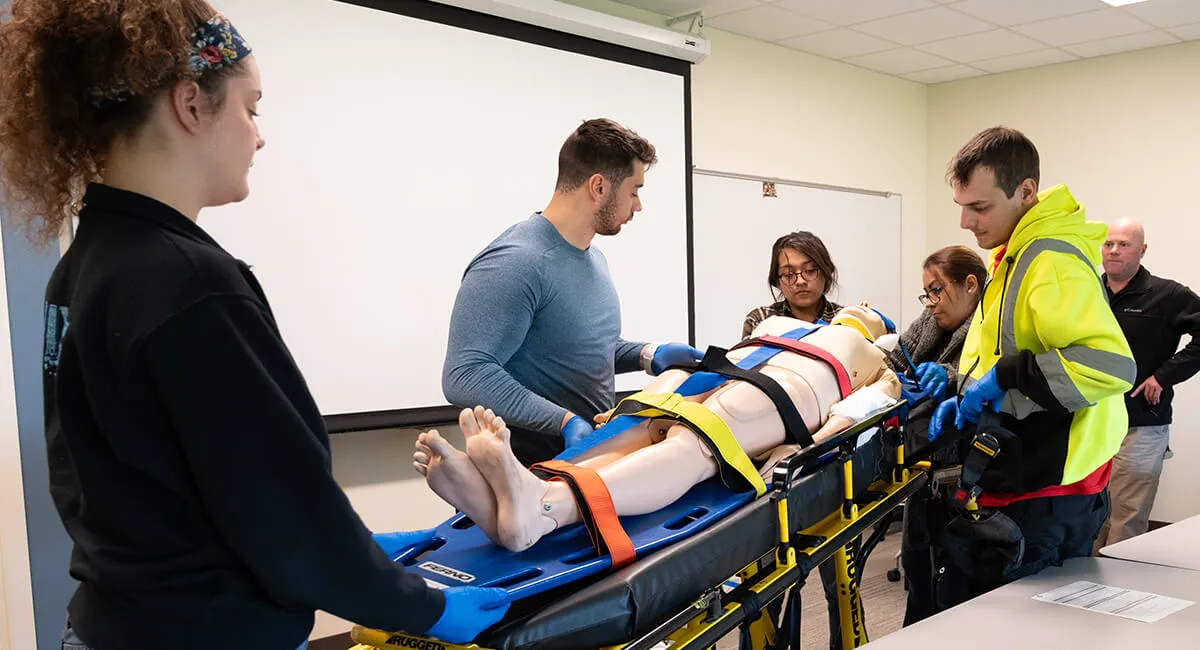 Students working with a training manikin on a gurnee.