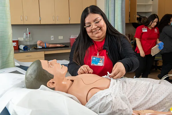 Un estudiante de formación en el área de la salud practica un procedimiento médico en un simulador de paciente en un aula clínica.