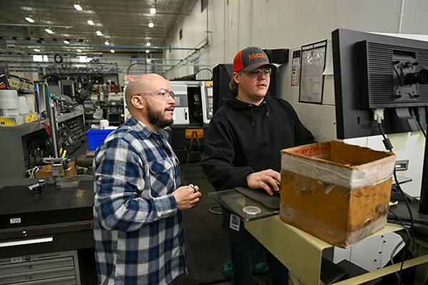Un estudiante y un instructor revisan juntos los controles de los equipos dentro de una planta de fabricación.