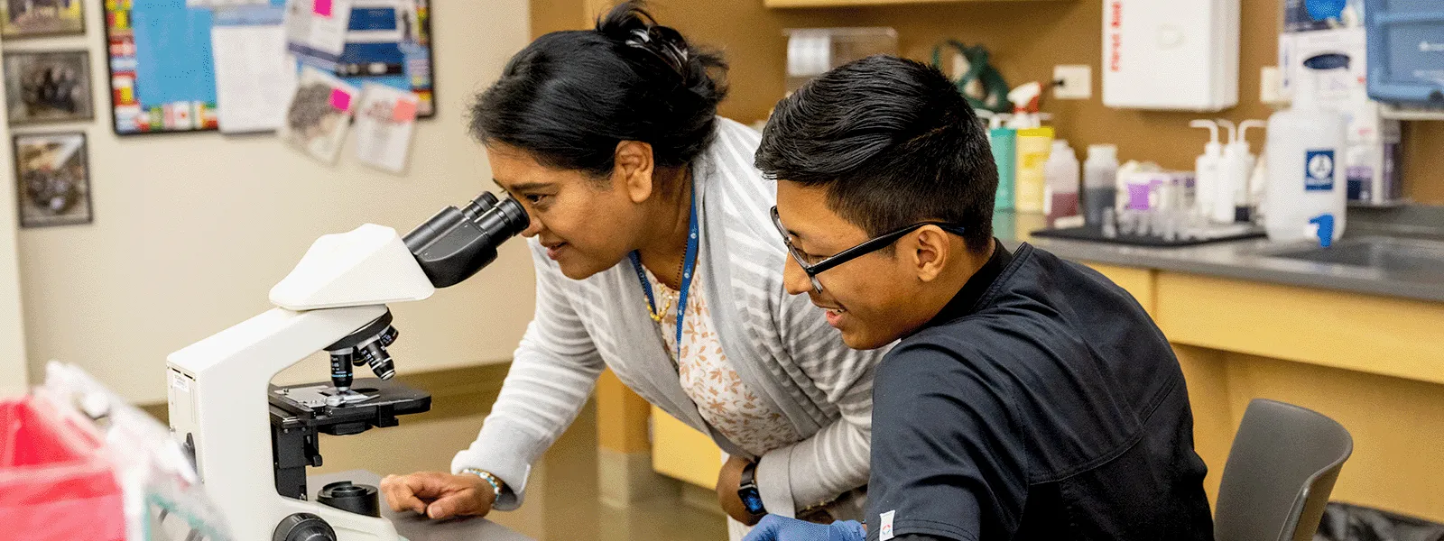 Professor looks through a microscope as student observes