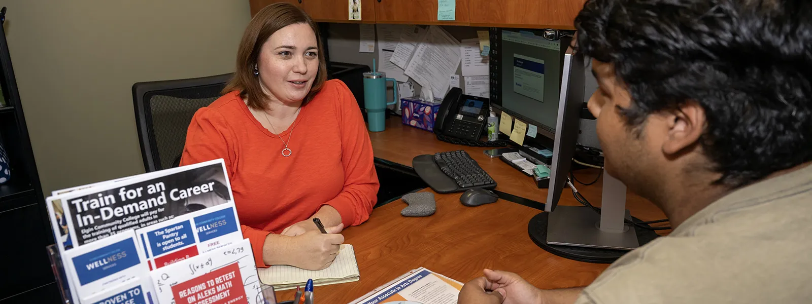 A student works with an advisor at a desk with a computer nearby