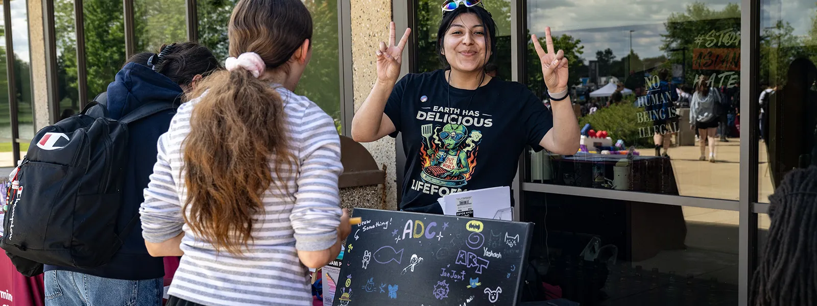 Students at a table promote the art and design club with a blackboard and chalk markers