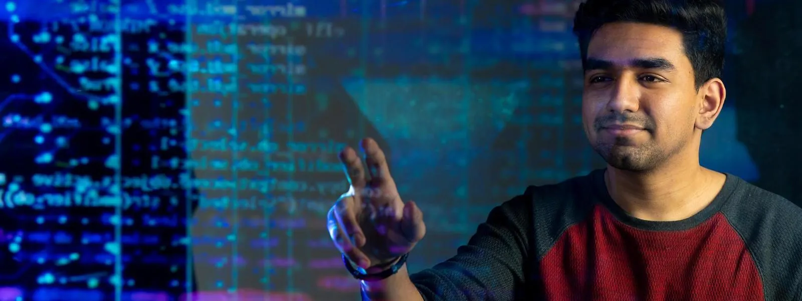 Male student interacting with digital interface on projected monitor in dark lit classroom.