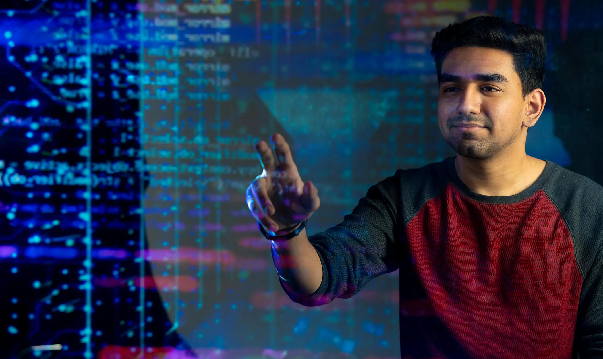 Estudiante varón interactuando con una interfaz digital en un monitor proyectado en un aula a oscuras.
