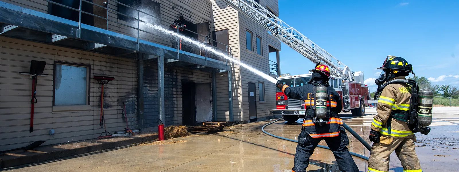 Two firefighters hose the side of a fire-damaged building.