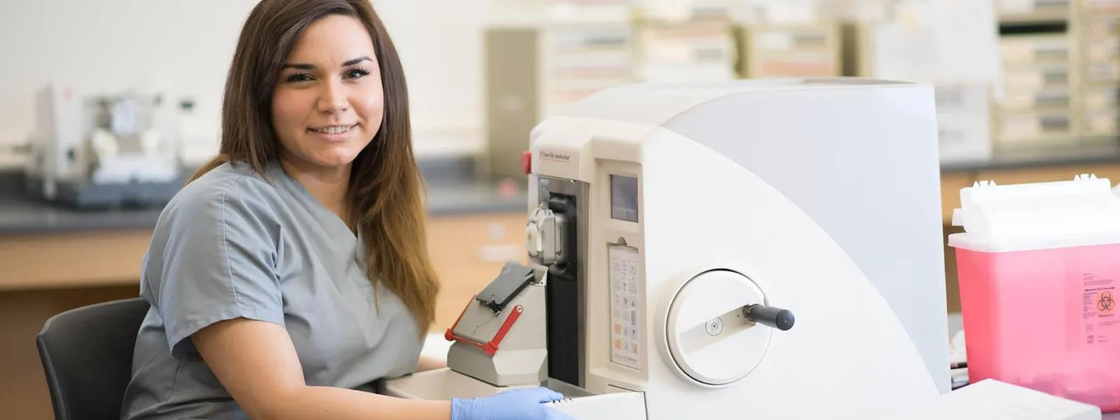 Histotechnology student sitting in front of a manual rotary microtome machine.