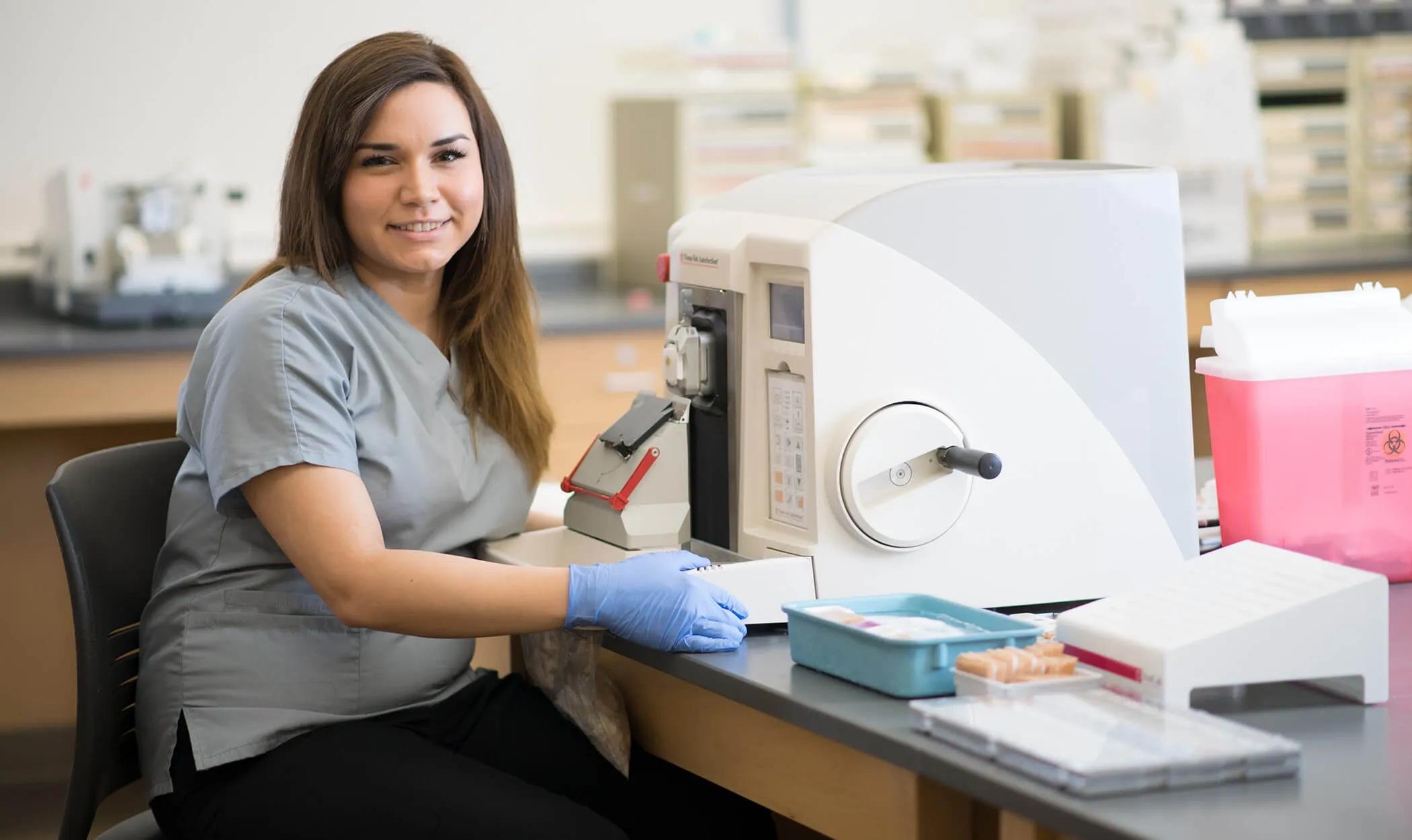 Histotechnology student sitting in front of a manual rotary microtome machine.
