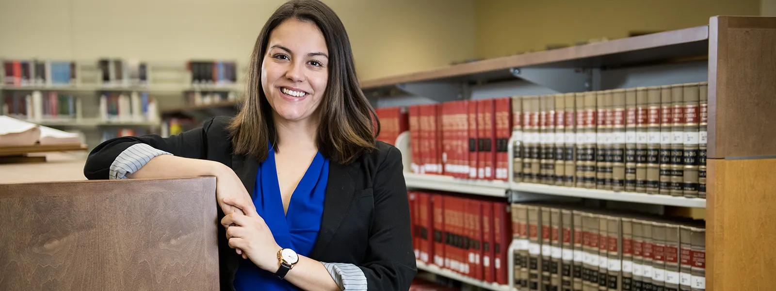 a student leaning against a bookcase with law books in the background