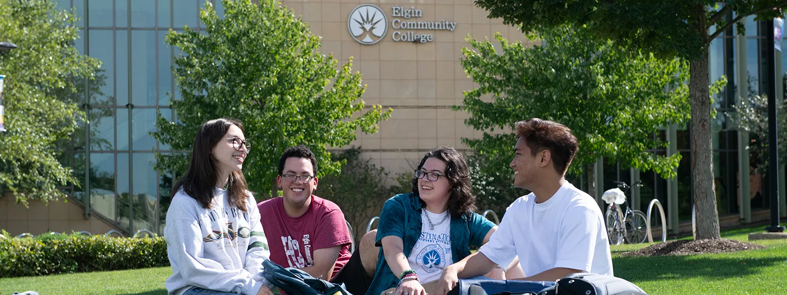 4 ECC students sitting in the lawn and talking in front of the library