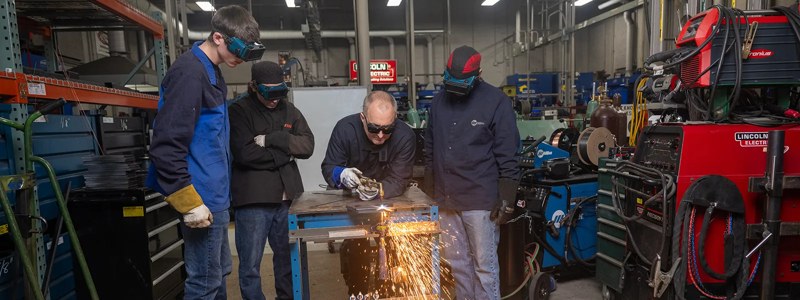 Students observe a professor welding material.