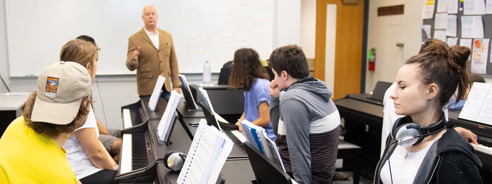 An ECC music professor instructing students seated at pianos