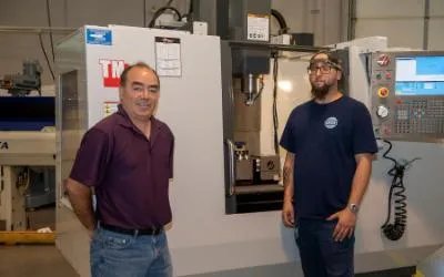 Professor Umberto Tinajero and student Steven Spicer stand in front of Computer Numerical Control (CNC) Machine