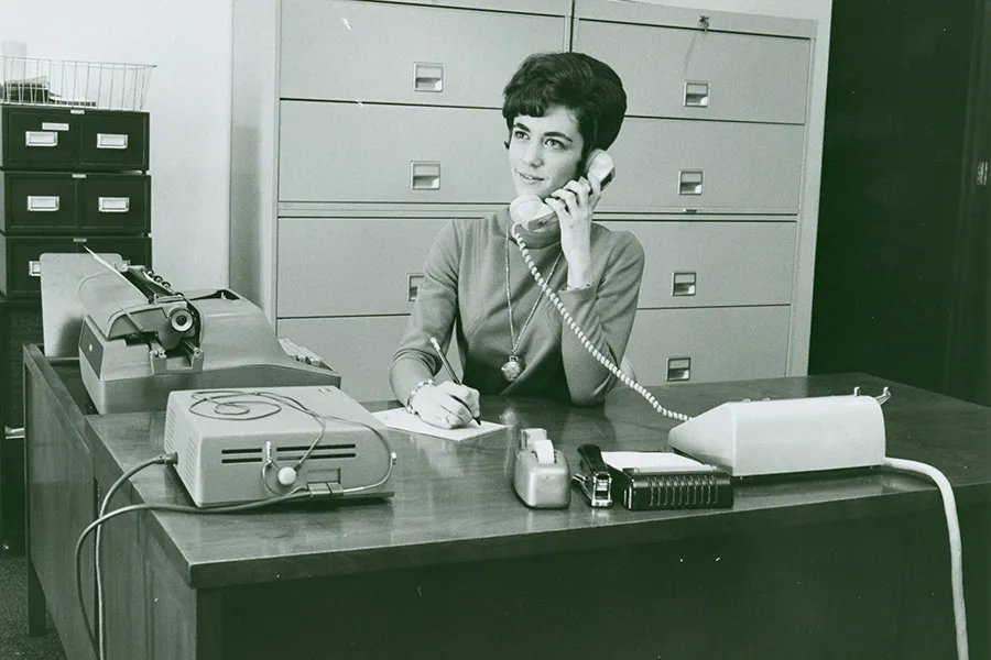 an administrative assistant sitting at a desk answering a phone
