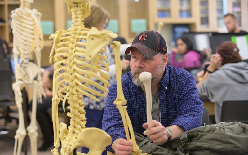 Un estudiante examina en una mesa de laboratorio el modelo de esqueleto de anatomía humana.