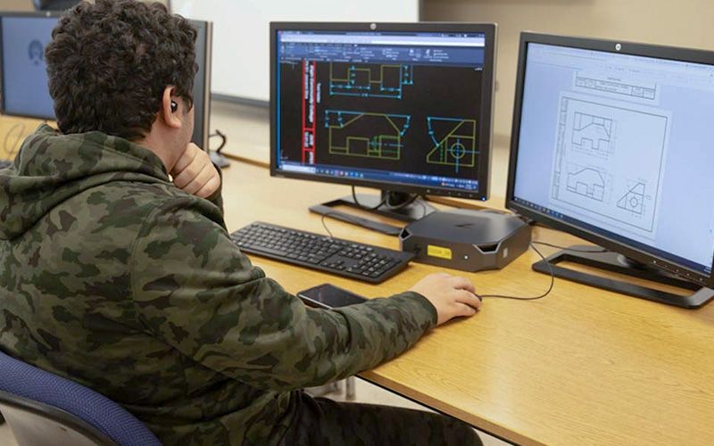 A male student is seated at a computer working on a CAD design.
